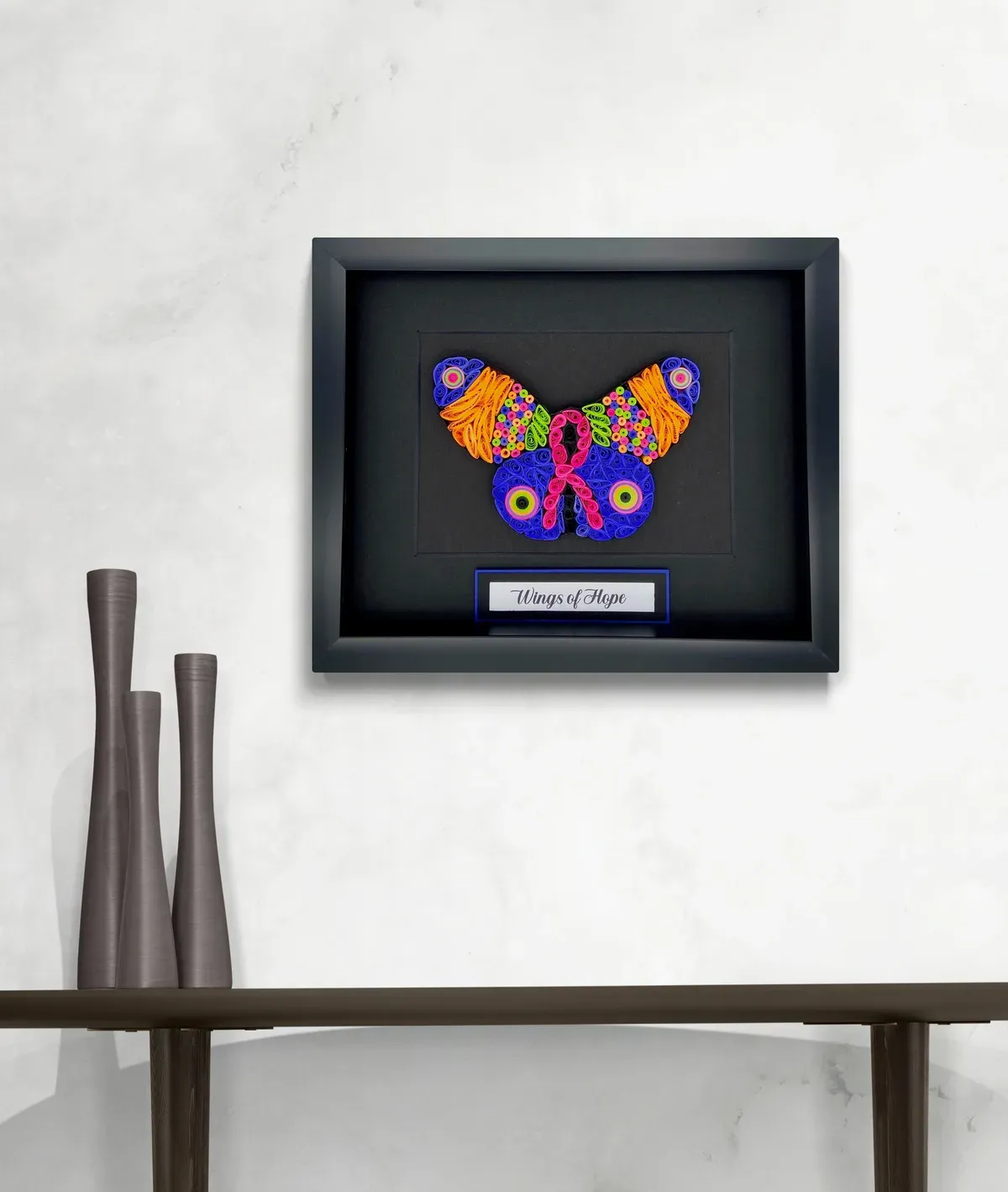 A framed, colorful butterfly artwork on a white wall above a wooden table.