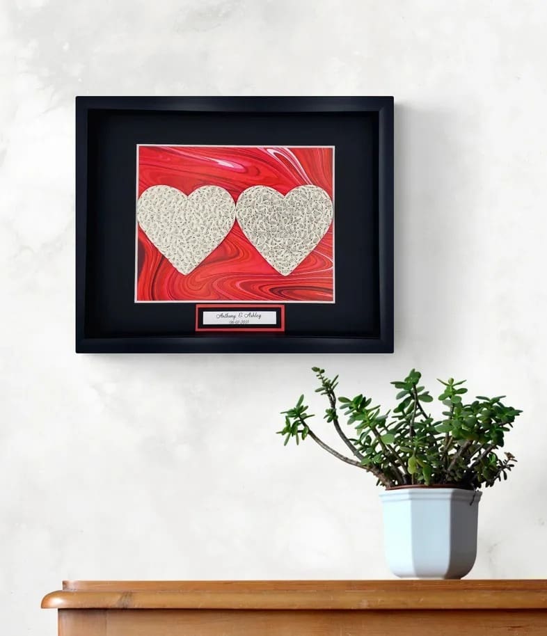 Framed double heart art on a wall above a potted plant.