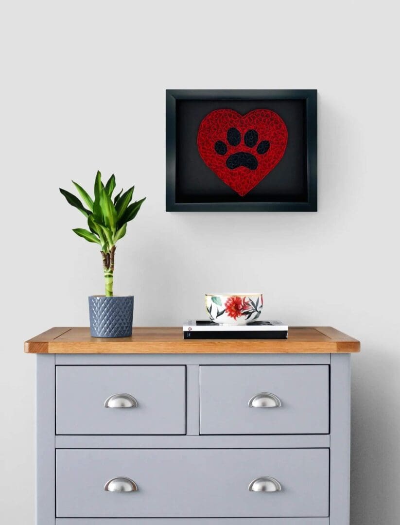 Cozy corner with a framed paw print, a green plant, and a minimalist gray cabinet.