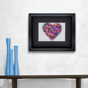 Framed colorful heart artwork above a wooden shelf with blue vases.