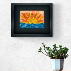 Framed colorful sun and ocean painting above a green plant in a white pot.