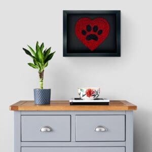 A framed red and black paw print art above a gray cabinet with a plant and coffee cup.