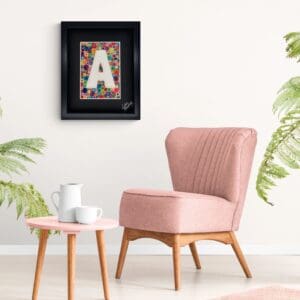 Cozy pink armchair with side table and framed letter 'A' on white wall.