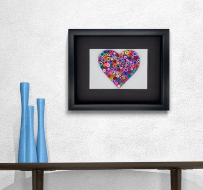 Framed heart artwork with vibrant floral design above a wooden table with blue vases.